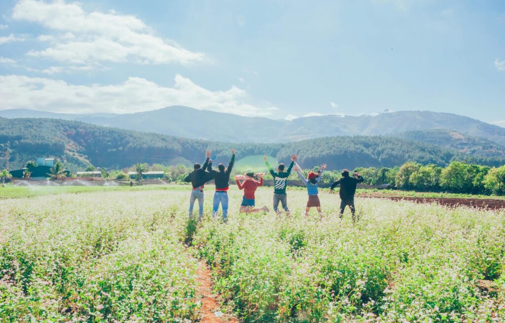 A group of friends joyfully celebrates in a vibrant countryside field with hills and bright skies.